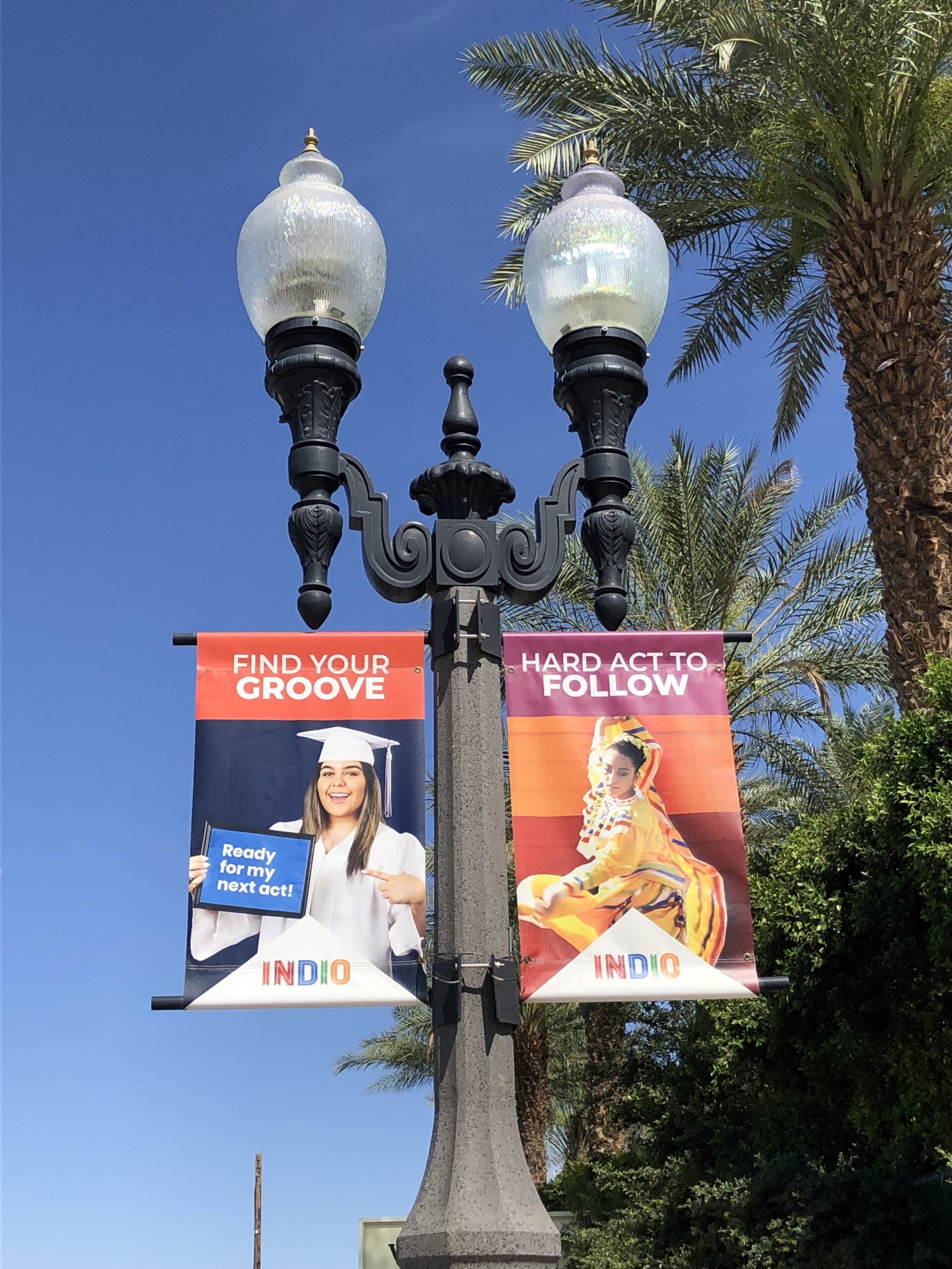 Pole banners in Indio, CA that feature a graduate and the text "Find Your Groove" and another featuring a dancer with the text "Hard Act To Follow".