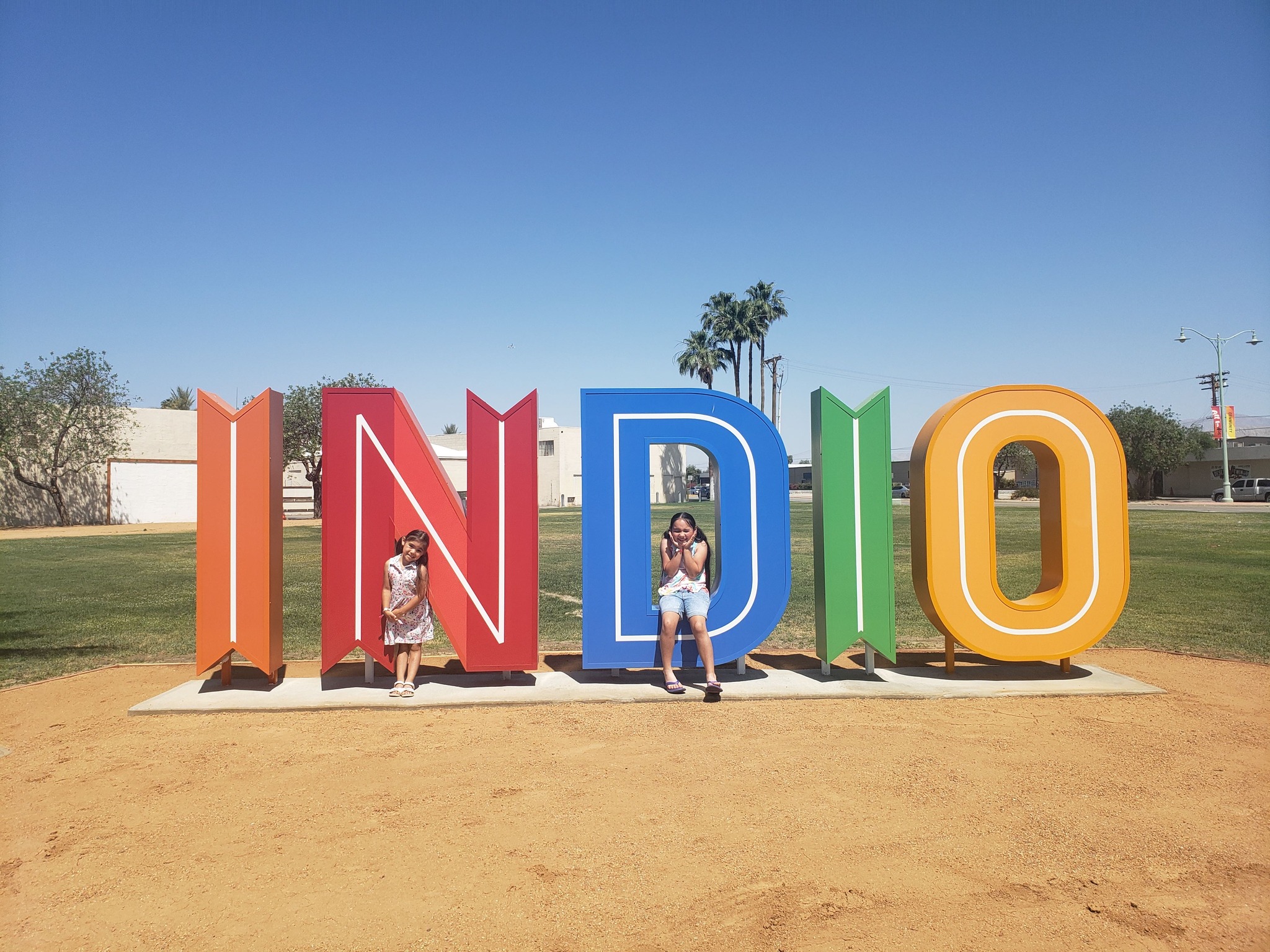 Two young girls pose in front of large outdoor INDIO signage.
